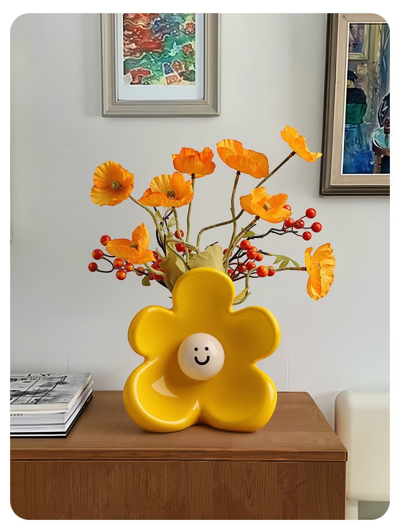 HOMELIVY yellow ceramic flower-shaped vase with a cute smiley face center, holding orange poppies on a wooden table.