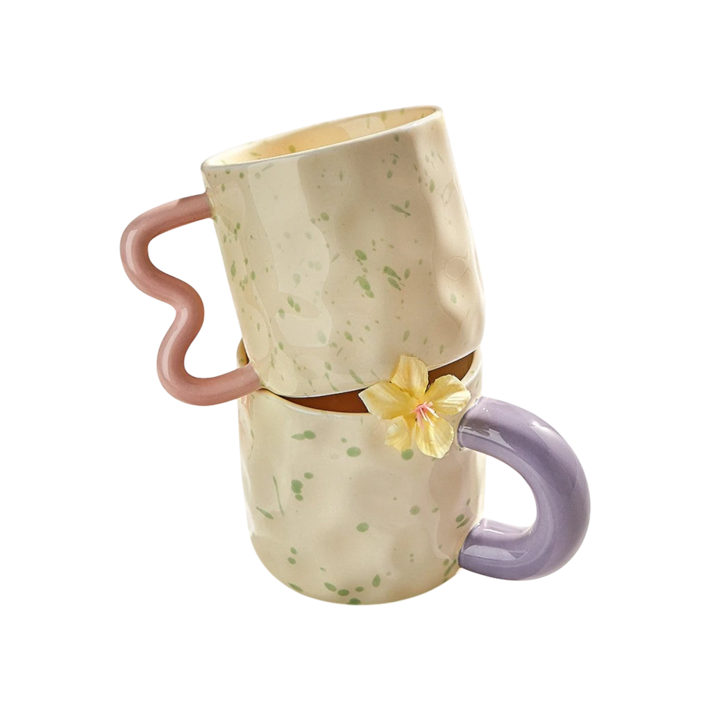 HOMELIVY cream speckled ceramic mugs with wavy pink and purple handles stacked on a white surface with flowers.