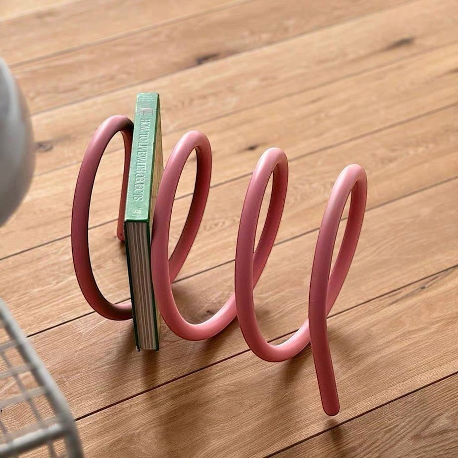 HOMELIVY pink spiral book holder with a sculptural spring-wave design holding a book on a wooden floor.