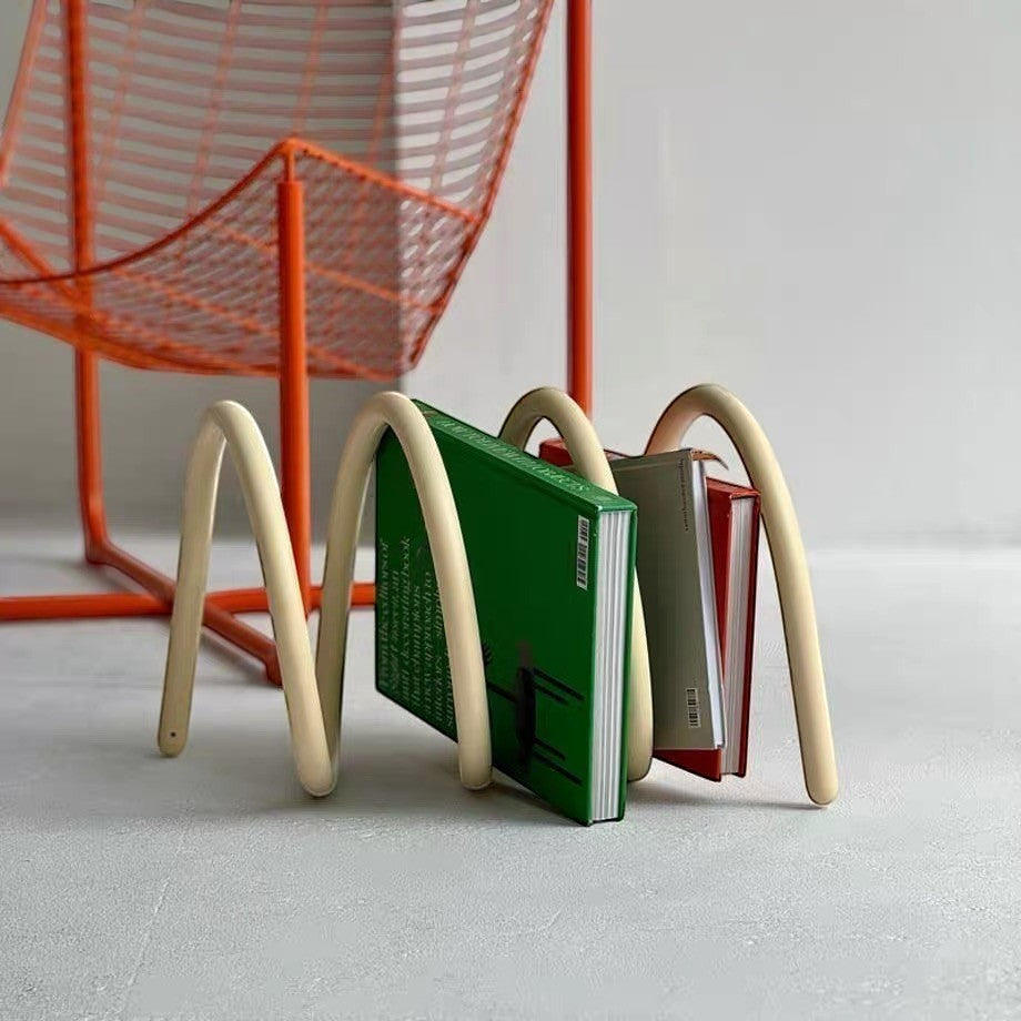 HOMELIVY cream spiral spring book holder displaying books on a grey floor with an orange wire chair in the background.