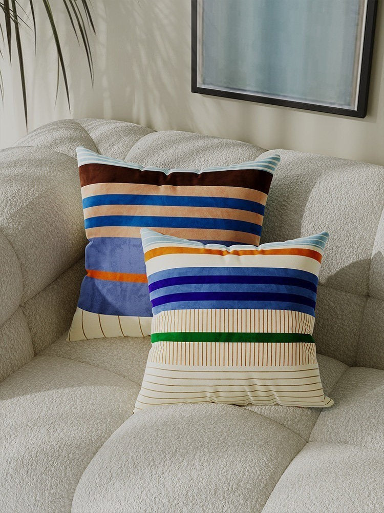 Dopamine colour block stripe cushion covers in velvet with blue, orange, and cream tones on a textured sofa.