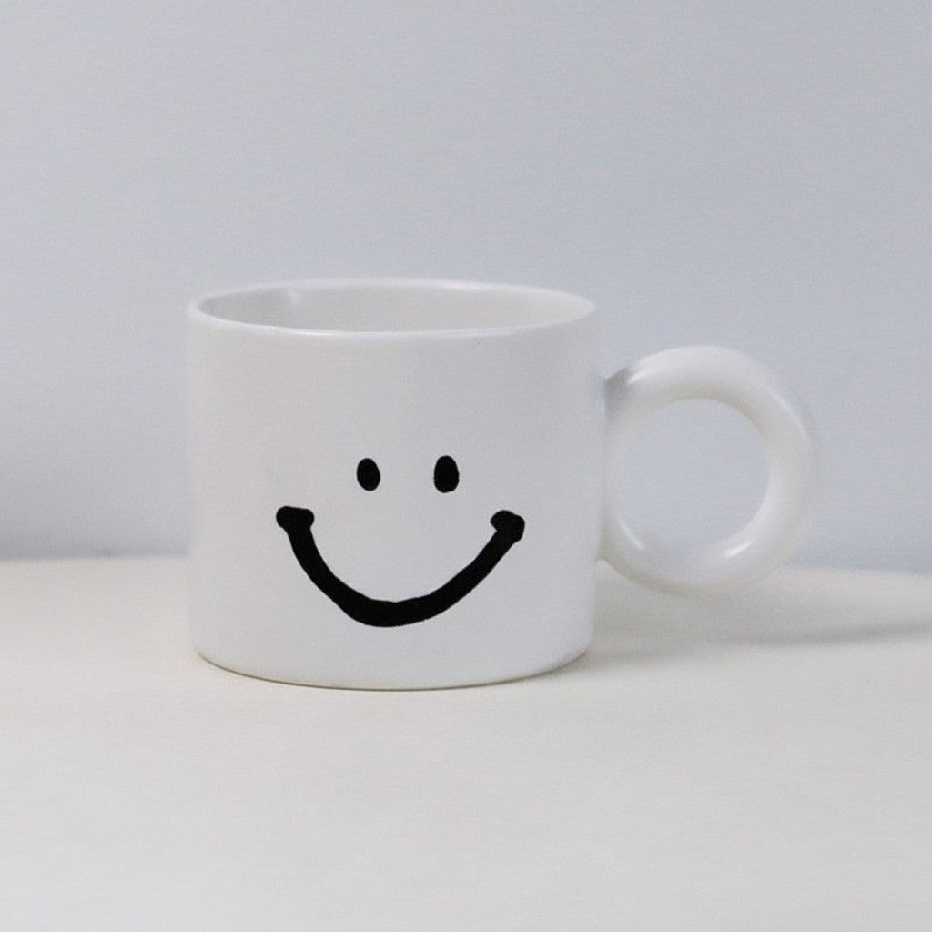 HOMELIVY white ceramic mug featuring a minimalist black smiley face design with a round handle.