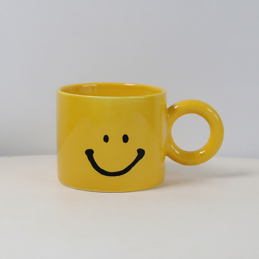 HOMELIVY yellow ceramic mug featuring a black smiley face design and a unique round handle on a white surface.