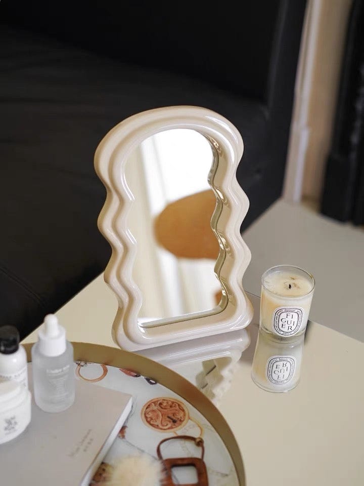 A cream-colored table squiggly mirror with wavy edges and a glossy ceramic finish for vanity use