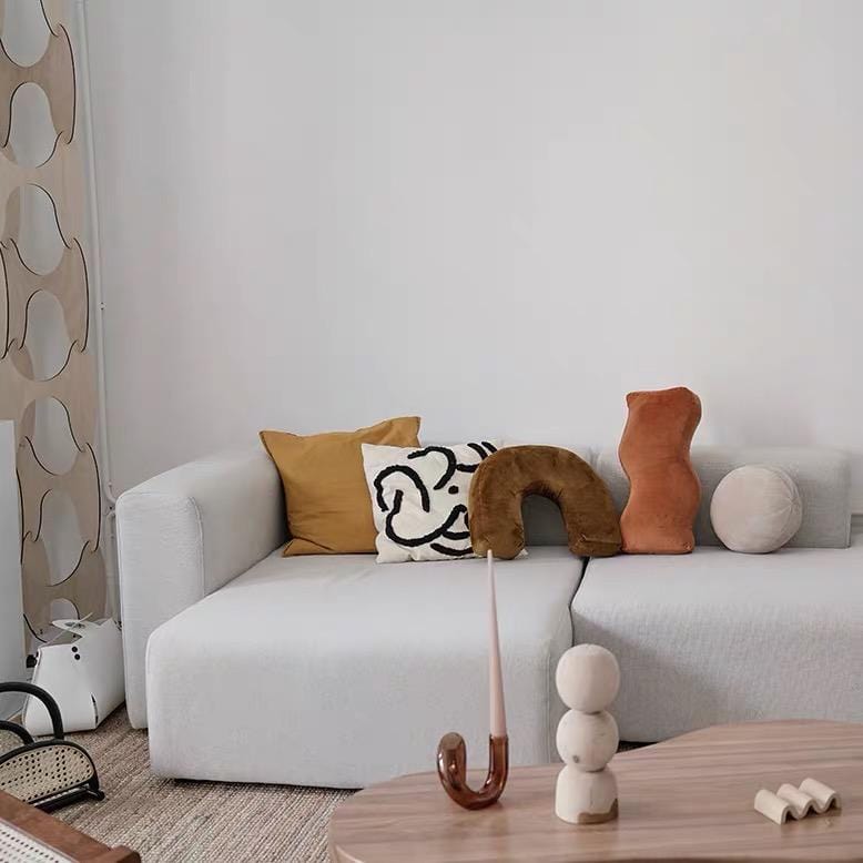 A minimalist white sofa featuring shaped plush cushions in mustard yellow, black and white abstract, and brown velvet