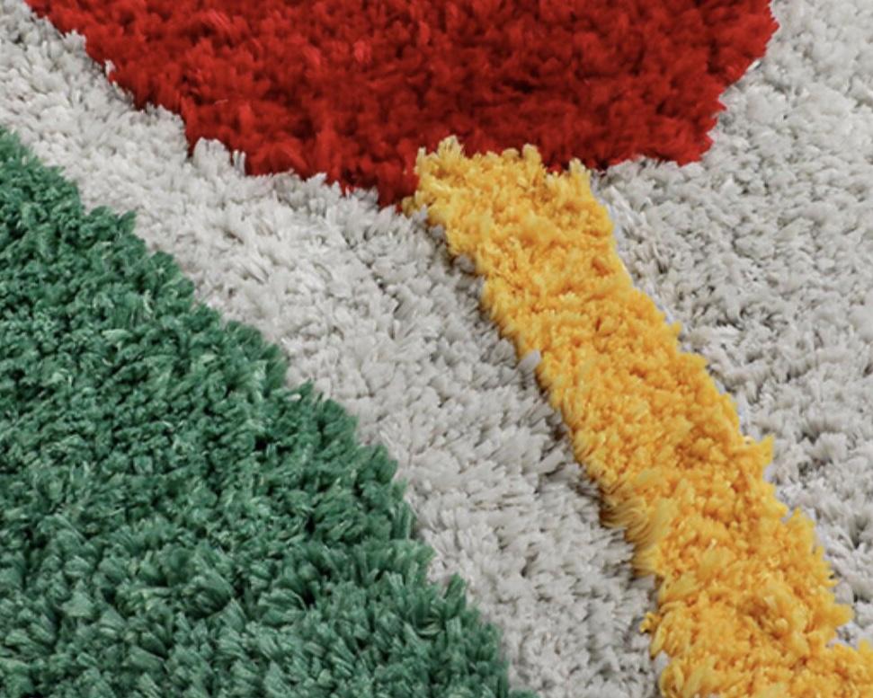 A plush shaggy red rose flower rug with bold geometric sections in red green yellow and gray colors