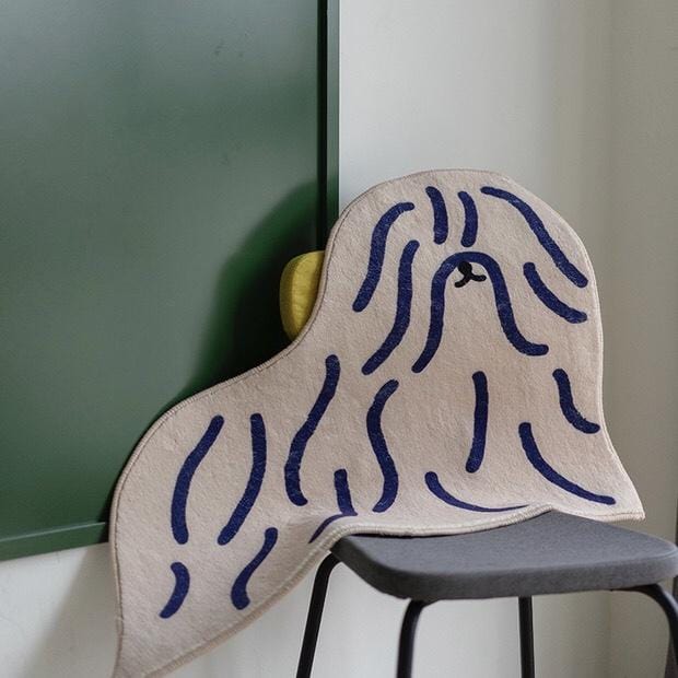 Beige plush cushion shaped like a dog with navy blue wavy line detailing in shaggy puppy dog rug design