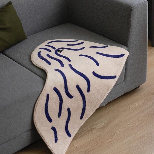 Beige shaggy puppy dog rug with navy blue wavy line pattern shaped like a stylized whale tail