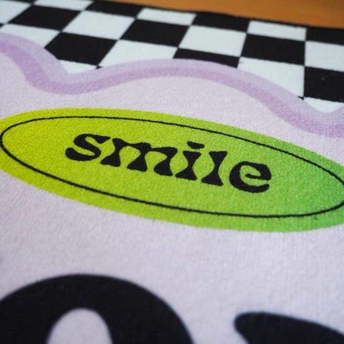 A soft plush white rug called Smile You Look Good featuring a lime green oval with smile in bold black and lavender border