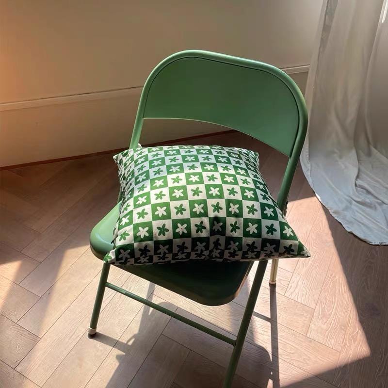 A green metal folding chair with a cushion featuring a black and white checkered floral throw pillow case