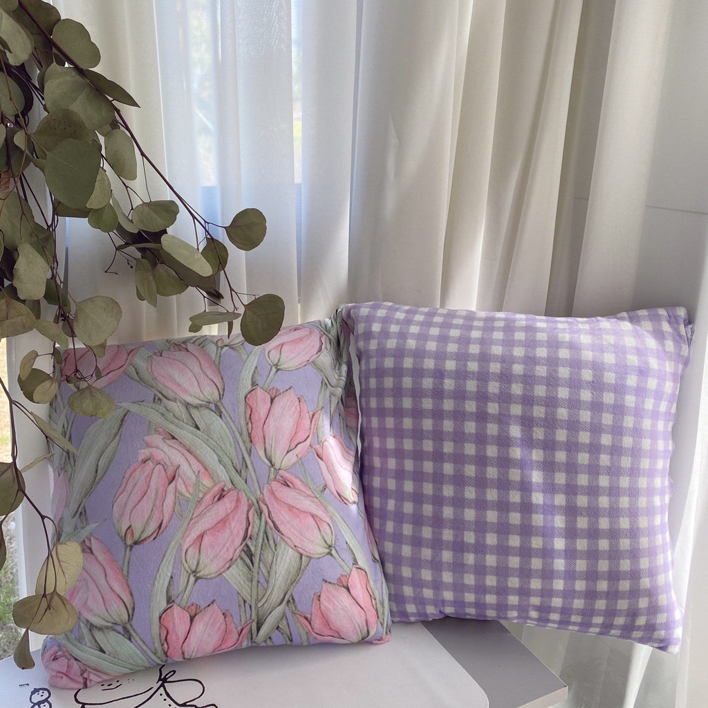 A pastel purple gingham plaid throw pillow with soft fabric texture next to a lavender pillow with pink tulip floral pattern