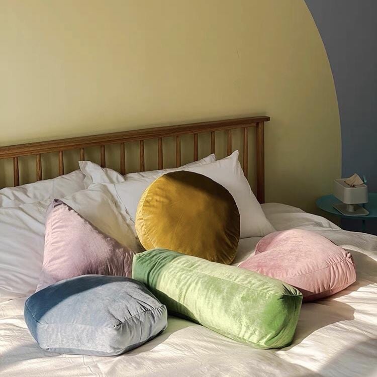 A collection of plush velvet geometry throw pillows in soft pastel and mustard hues arranged on a bed